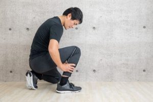 アキレス腱炎に悩みながらも、ランニングに出かけようとして、アキレス腱の痛みに顔をしかめる日本人男性