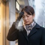駅から寒い屋外に出て頭痛を感じ額に手を当てる日本人女性会社員
